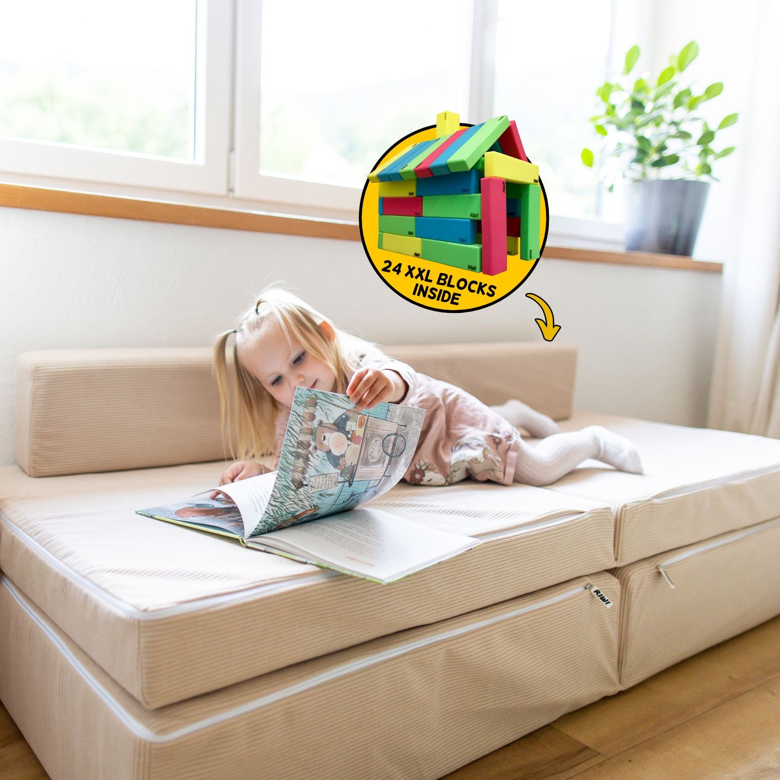 Child reading a book on a beige play mat with colorful blocks inset