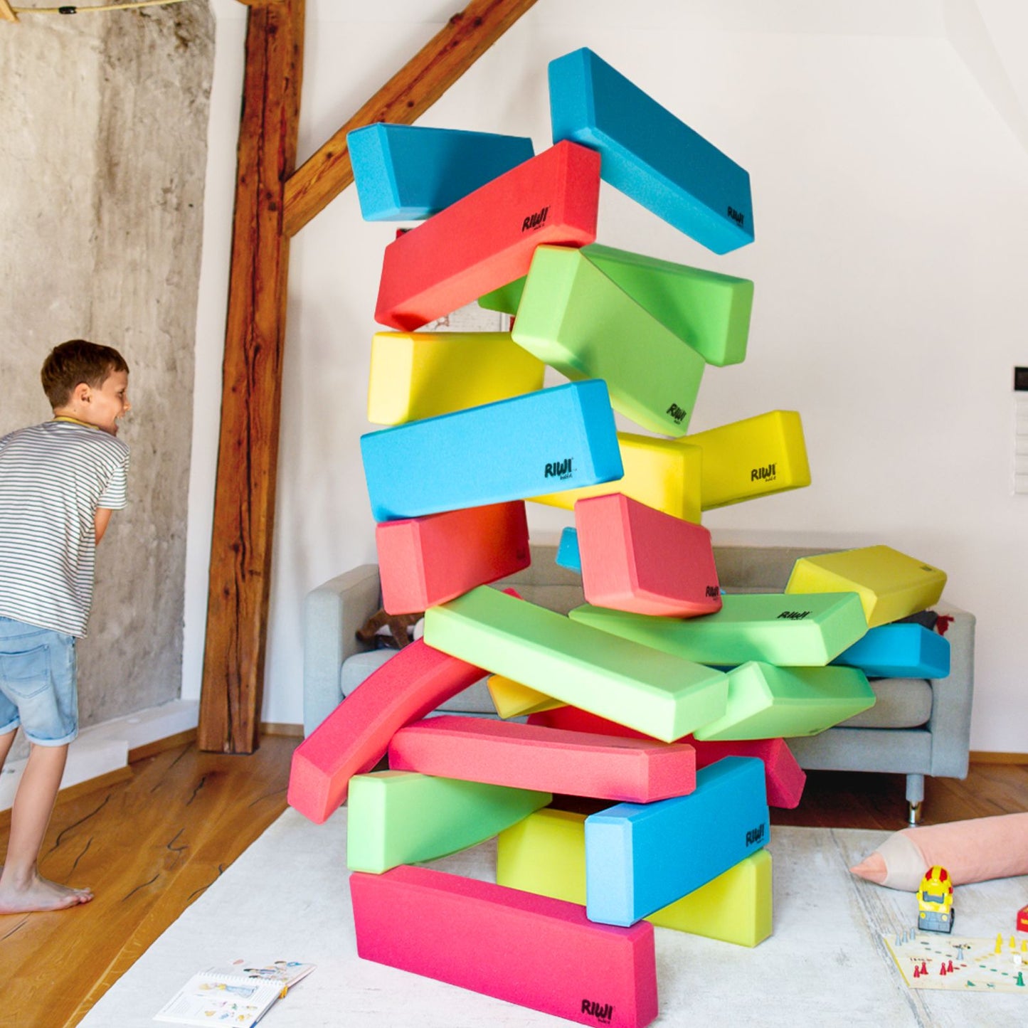 Colorful foam blocks stacked into a tower with a child in the background RIWI blocks